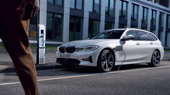 Plug-In Hybrid BMW 3er Touring 2021 G21 Dreiviertel-Frontansicht ladend Plug-In Hybrid BMW 3er Touring 2021 G21 Dreiviertel-Frontansicht ladend vor Gebäude