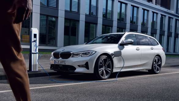 Plug-in Hybrid BMW 3er Touring 2021 G21 Dreiviertel-Frontansicht ladend Plug-in Hybrid BMW 3er Touring 2021 G21 Dreiviertel-Frontansicht ladend vor Gebäude