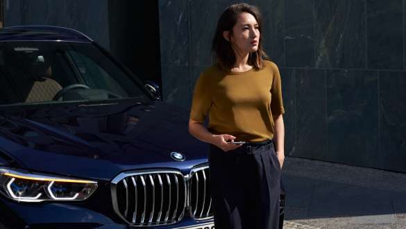 BMW Pannen- und Unfallhilfe BMW Pannen- und Unfallhilfe Frau mit Smartphone vor einem BMW