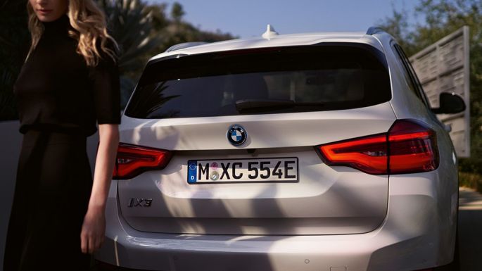 Heck mit BMW i spezifischem Diffusor BMW iX3 G08 Heckansicht mit Frau Heck mit BMW i spezifischem Diffusor BMW iX3 G08 2020 Mineralweiß metallic Heckansicht mit Frau