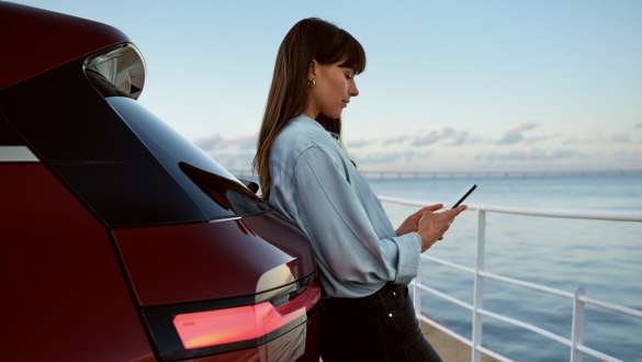 My BMW App BMW Reparaturen und Pflege BMW Reparaturen und Pflege My BMW App Frau mit Smartphone in den Händen lehnt an BMW Fahrzeug