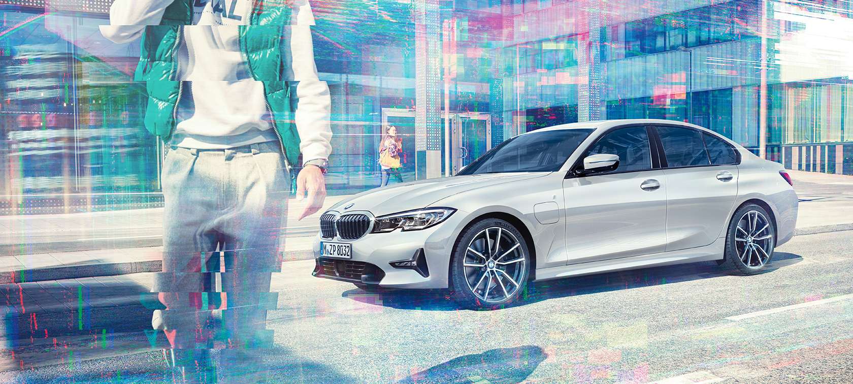BMW 3er Limousine, Seitschuss BMW 330e. Dreiviertel-Seitschuss der stehenden BMW 330e Limousine vor urbanem Glasgebäude mit sich bewegenden Passanten.