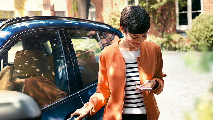 BMW Paket Care Frau mit Smartphone an der Tür ihres BMW BMW Paket Care Frau mit Smartphone an der Tür ihres BMW