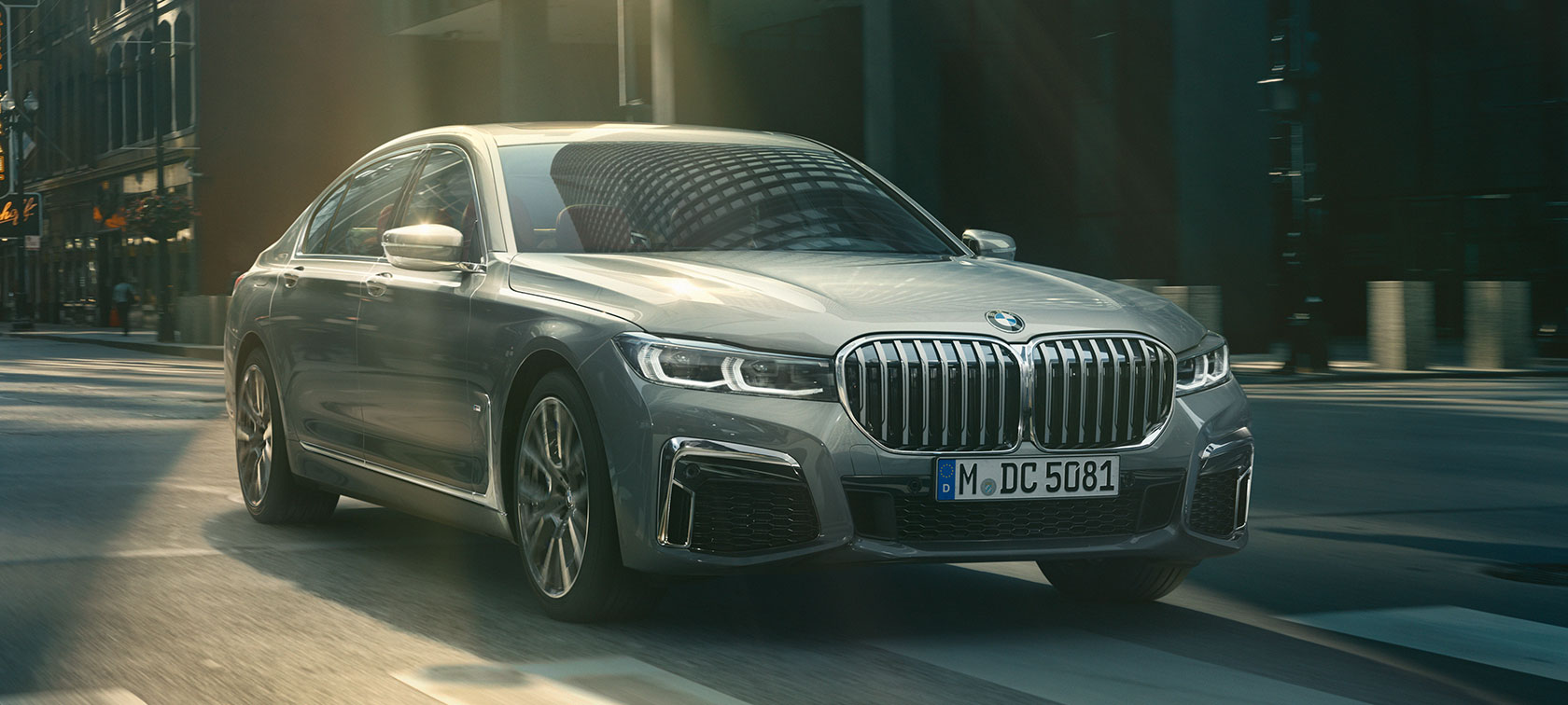 Graue BMW 7er Limousine fahrend, Dreiviertelfrontansicht Graue BMW 7er Limousine fährt in der Dreiviertelfrontansicht durch urbane Kulisse