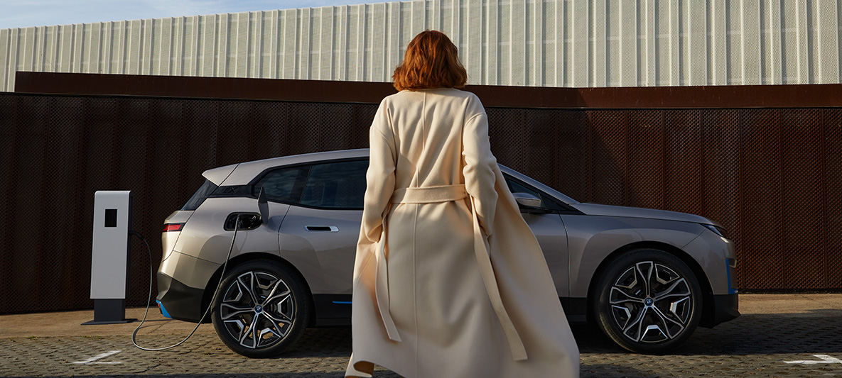 BMW iX Seitenansicht stehend BMW iX Kaschmirsilber i20 Seitenansicht stehend mit Model davor