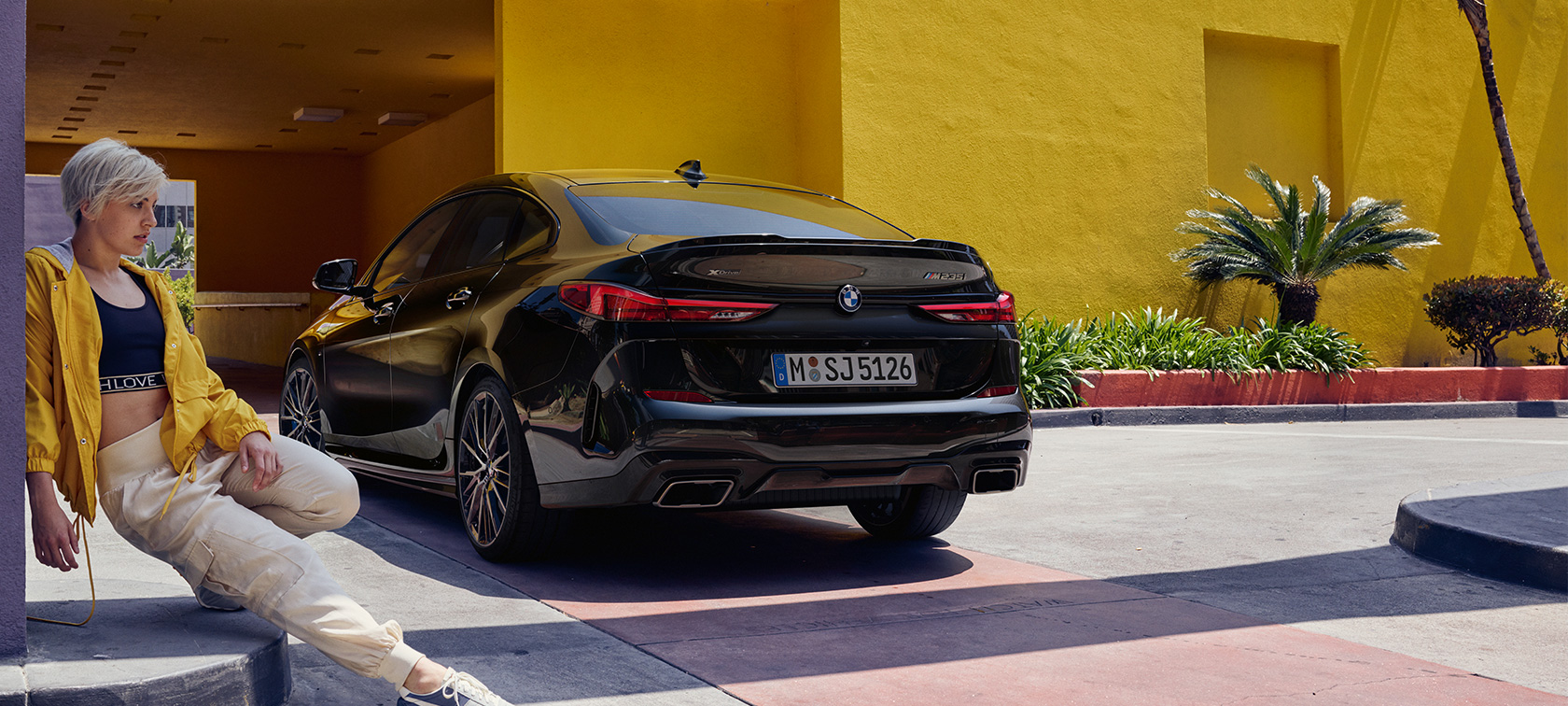 BMW M235i xDrive Gran Coupé Dreiviertel-Heckansicht BMW M235i xDrive Gran Coupé Black Sapphire metallic F44 Dreiviertel-Heckansicht mit Frau im Vordergrund