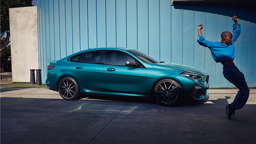 BMW M235i xDrive Gran Coupé F44 Seitenansicht mit Frau im Vordergrund BMW M235i xDrive Gran Coupé F44 Snapper Rocks Blau metallic Seitenansicht mit Frau im Vordergrund