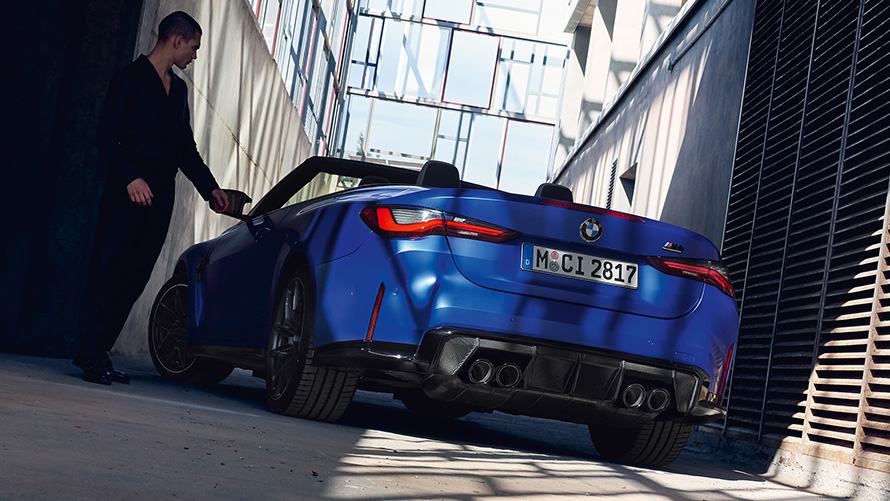 BMW M4 Competition Cabrio mit M xDrive G83 2021 Dreiviertel-Heckansicht BMW M4 Competition Cabrio mit M xDrive G83 2021 BMW Individual Frozen Portimao Blau metallic Dreiviertel-Heckansicht mit Mann