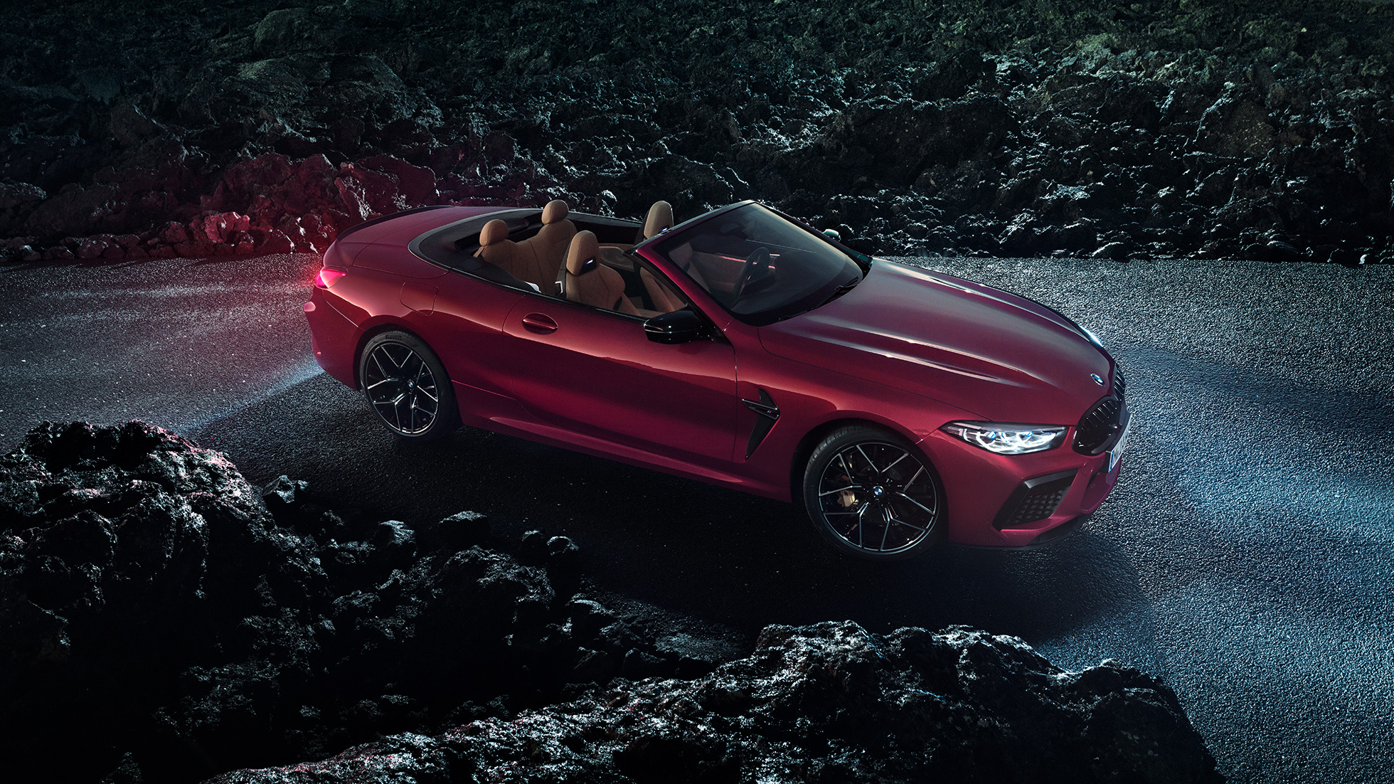 BMW M8 Competition Cabrio, Dreiviertel-Seitenansicht. BMW M8 Competition Cabrio in Motegi Rot metallic mit geöffnetem Verdeck, Dreiviertel-Seitenansicht, stehend bei Nacht auf Asphalt.