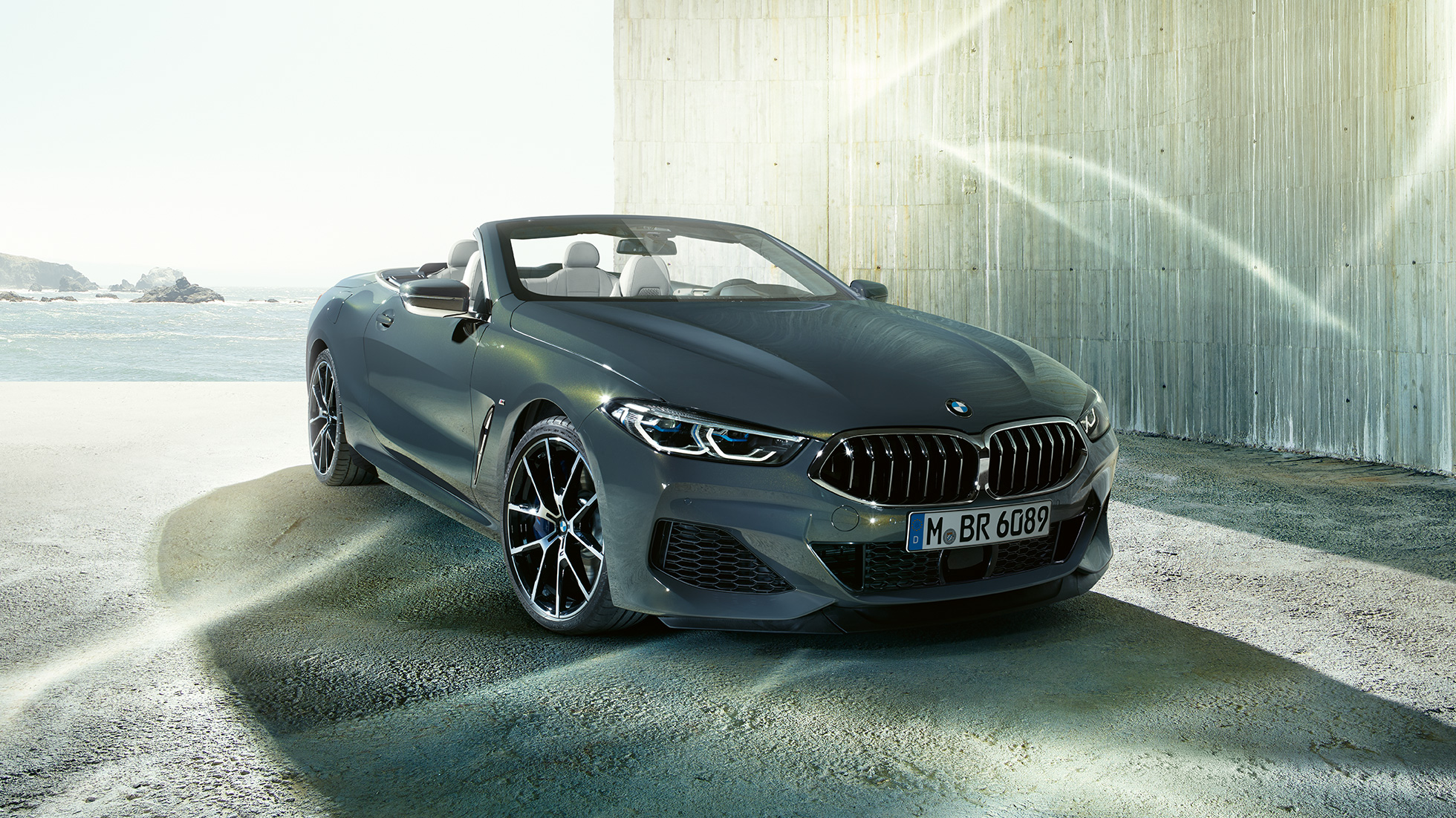 BMW M850i xDrive Cabrio, Dreiviertel-Frontansicht. BMW M850i xDrive Cabrio in Dravitgrau metallic mit geöffnetem Verdeck, Dreiviertel-Frontansicht, stehend vor Küste.