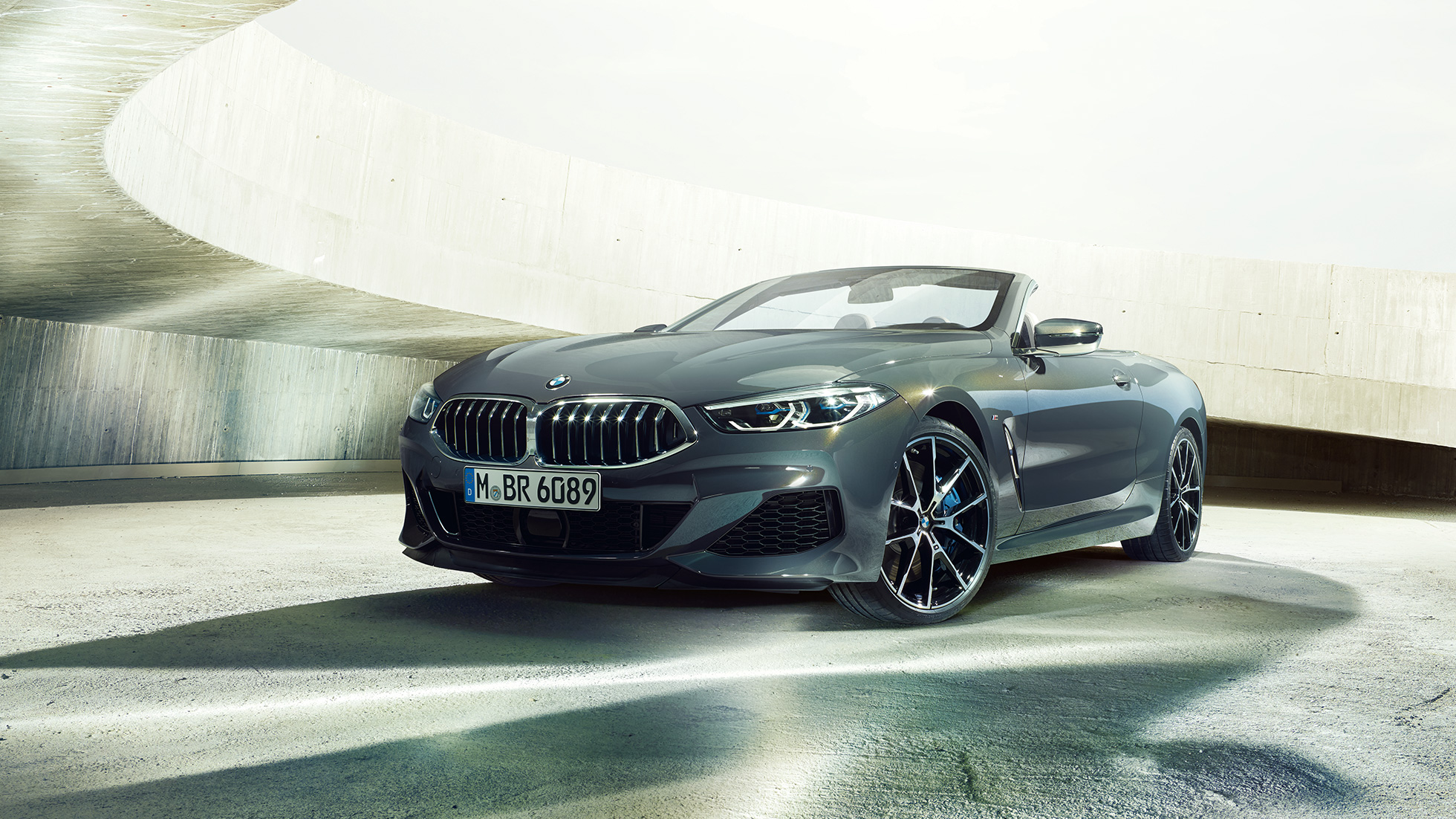 BMW M850i xDrive Cabrio, Dreiviertel-Frontansicht. BMW M850i xDrive Cabrio in Dravitgrau metallic mit geöffnetem Verdeck, Dreiviertel-Frontansicht, stehend in Betongebäude.