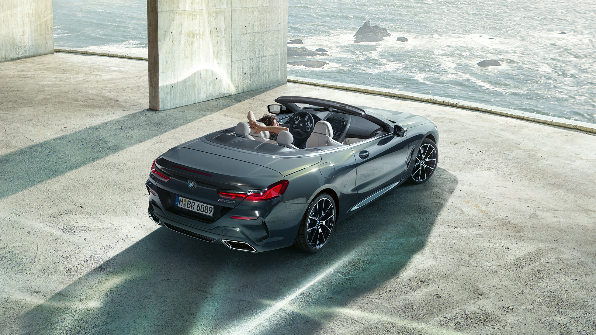 BMW M850i xDrive Cabrio, Vogelperspektive. BMW M850i xDrive Cabrio in Dravitgrau metallic mit geöffnetem Verdeck, Vogelperspektive, parkend in Betongebäude vor Ozean.
