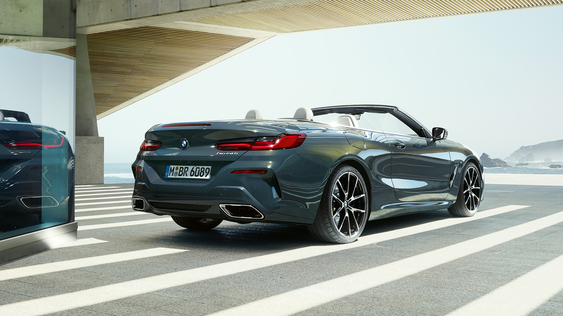 BMW M850i xDrive Cabrio, Dreiviertel Heckansicht. BMW M850i xDrive Cabrio in Dravitgrau metallic mit geöffnetem Verdeck, Dreiviertel Heckansicht, parkend mit Blick auf Ozean.