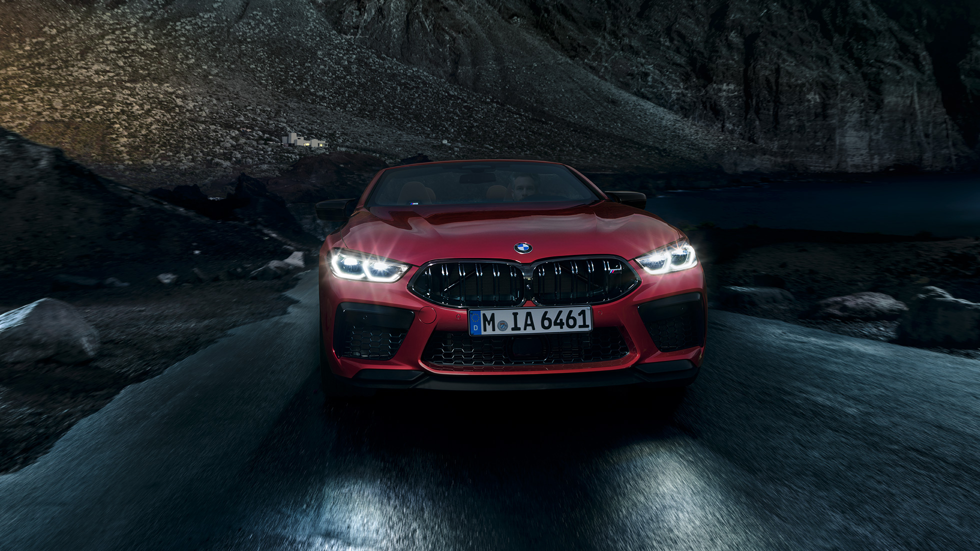 BMW M8 Competition Cabrio, Frontansicht. BMW M8 Competition Cabrio in Motegi Rot metallic mit leuchtenden Scheinwerfern, Frontansicht, fahrend bei Nacht.