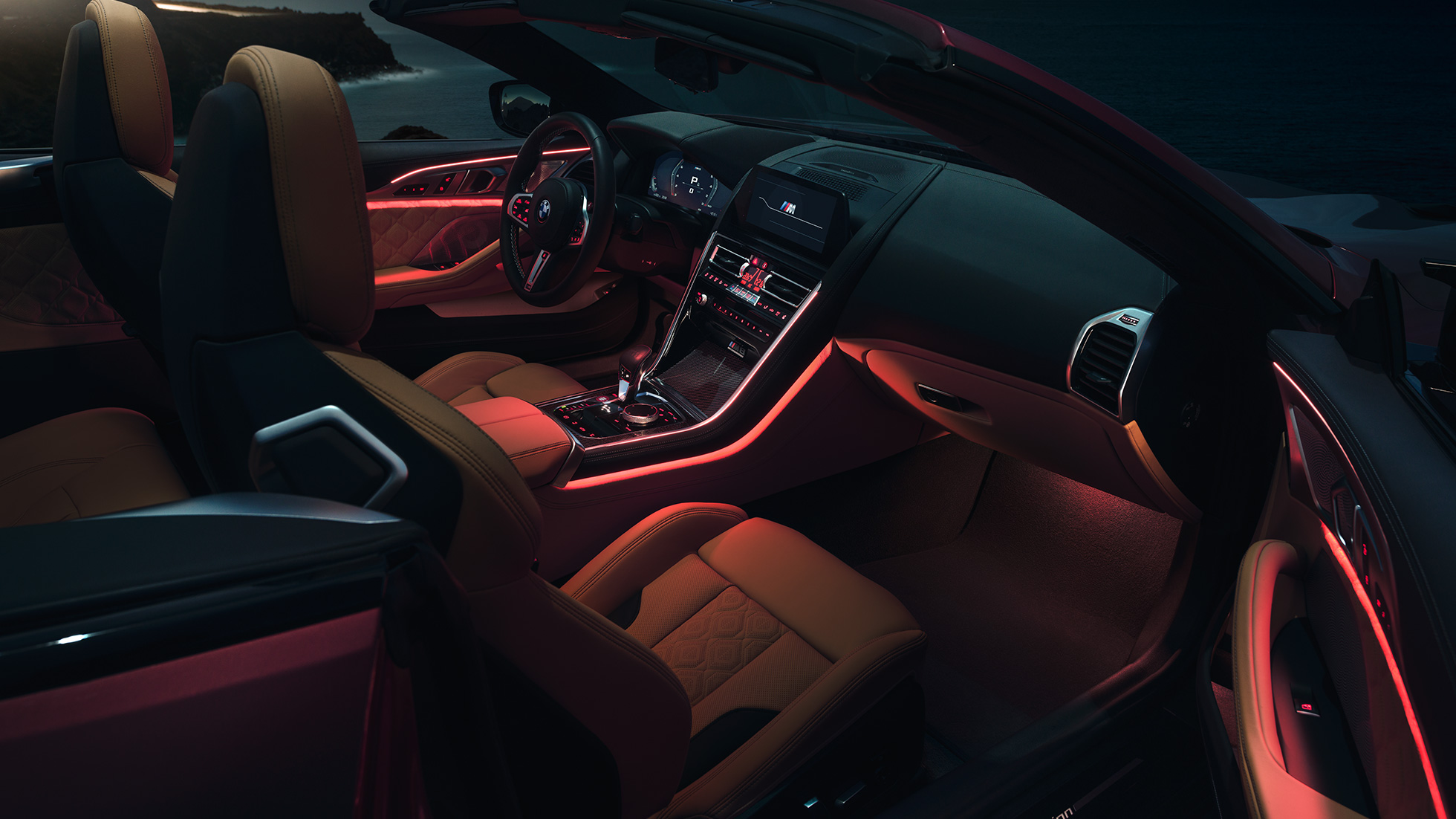 BMW M8 Competition Cabrio, Interieur. BMW M8 Competition Cabrio mit geöffnetem Verdeck, Interieur mit rotem ambienten Licht bei Nacht.