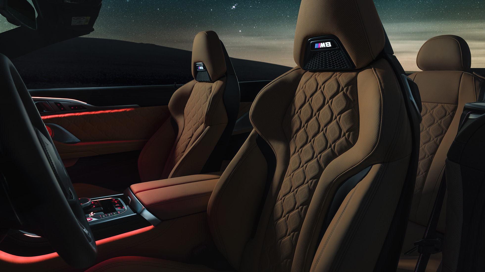 M Sportsitze in Leder 'Merino'. BMW M8 Competition Cabrio mit geöffnetem Verdeck unter Sternenhimmel, Innenraum mit M Sportsitzen in Leder 'Merino' und rotem ambienten Licht.