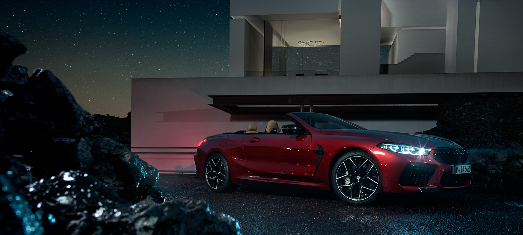 BMW M8 Competition Cabrio, Dreiviertel-Seitenansicht. BMW M8 Competition Cabrio in Motegi Rot metallic, Dreiviertel-Seitenansicht, stehend bei Nacht vor Villa.