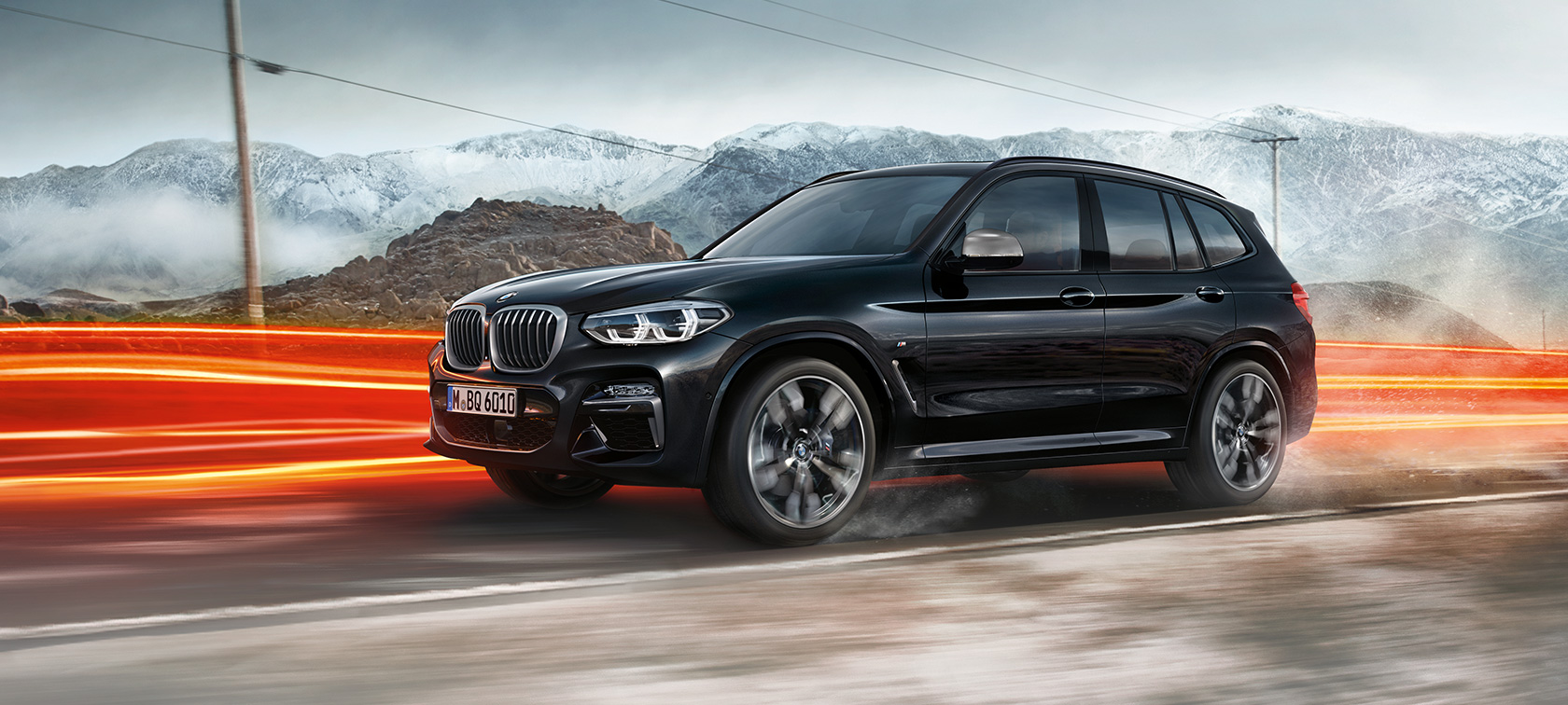 BMW X3 M40i und BMW X3 M40d, Seitenansicht. BMW X3 M40i und BMW X3 M40d in Saphierschwarz metallic, fahrend, Exterieur, Seitenansicht vor Berglandschaft mit Lichtstreifen.