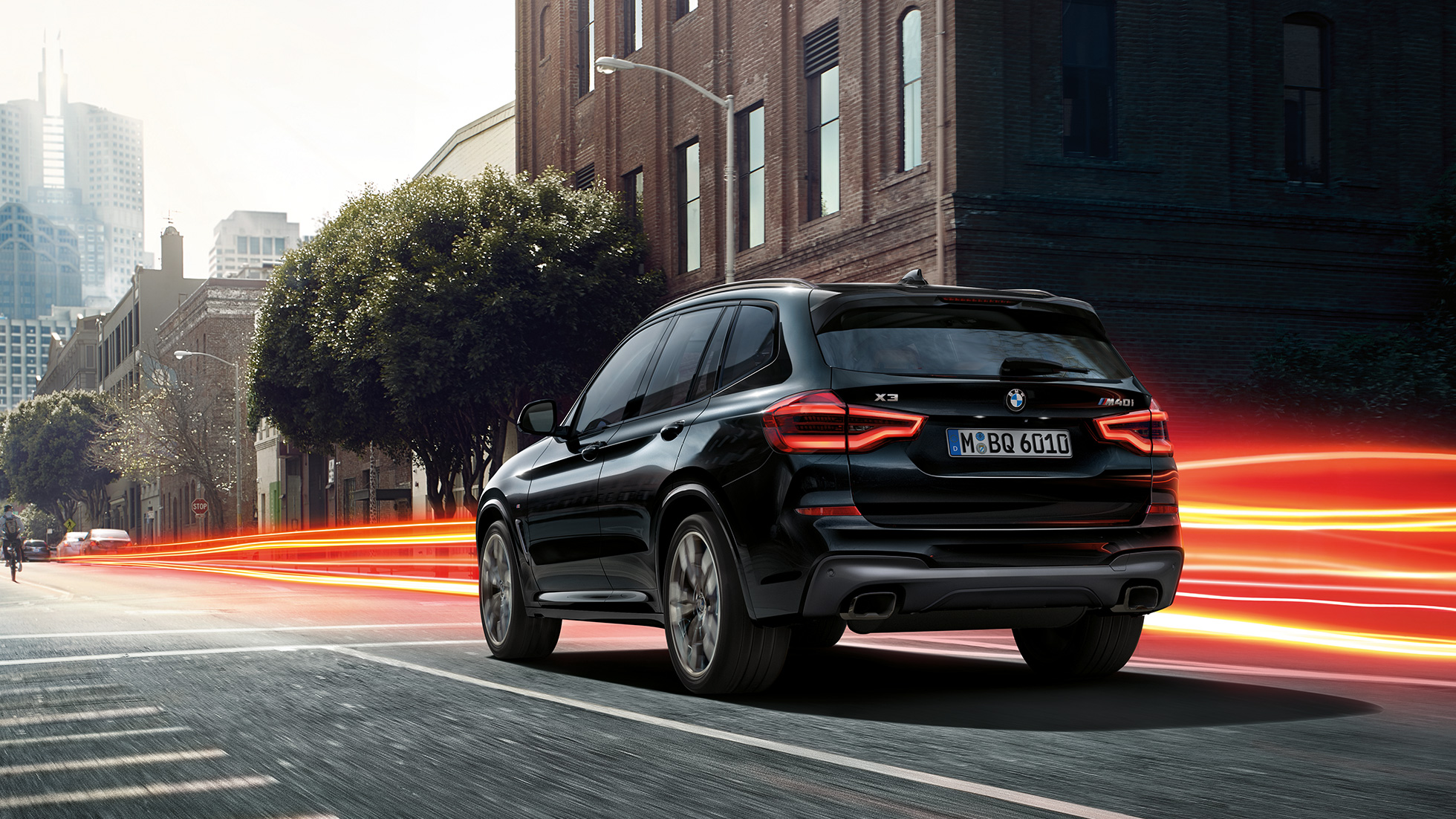 BMW X3 M40i, Dreiviertel-Heckansicht. BMW X3 M40i in Saphierschwarz metallic, fahrend, Exterieur, Dreiviertel-Heckansicht vor städtischer Kulisse mit Lichtstreifen.