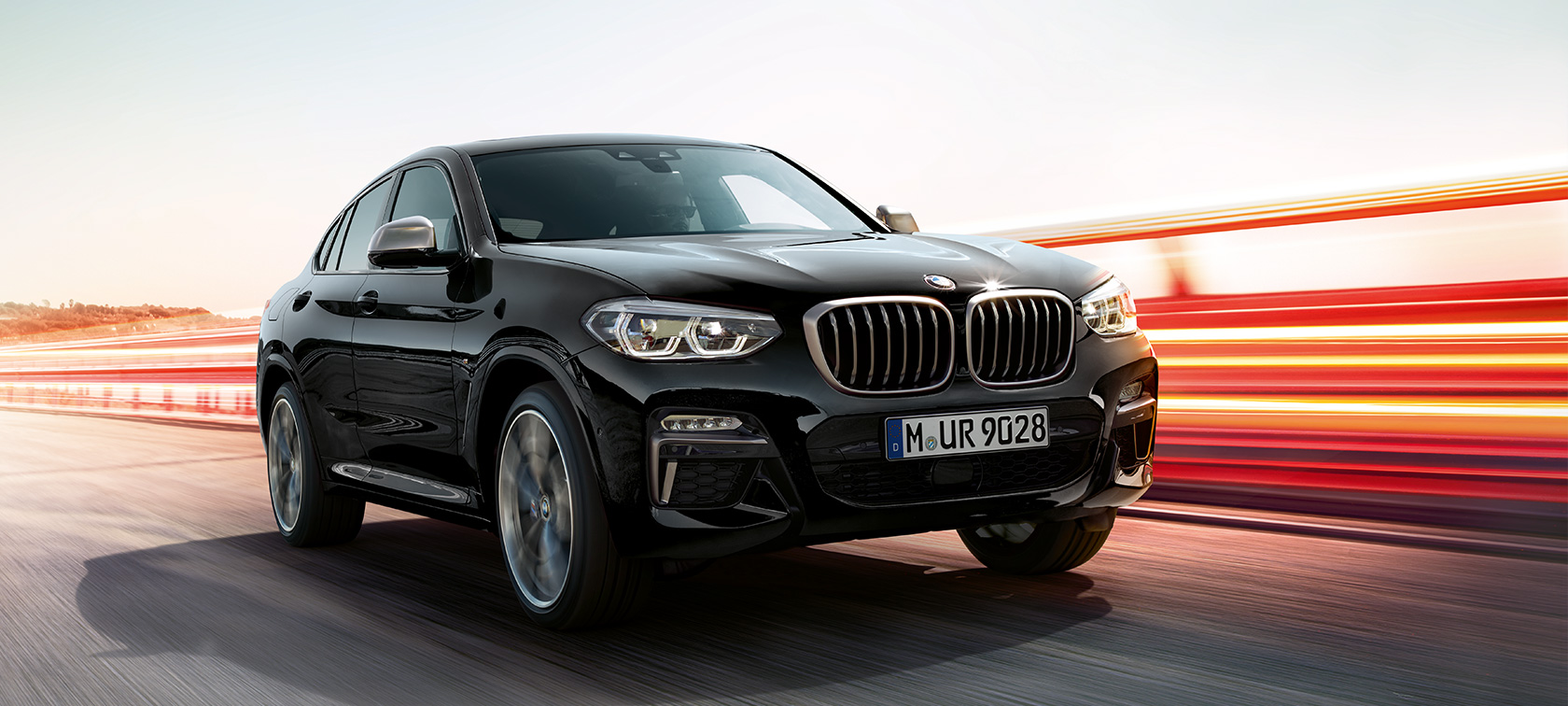 BMW X4 M40i und BMW X4 M40d, Dreiviertel-Frontansicht links. BMW X4 M40i und BMW X4 M40d in Saphierschwarz metallic, fahrend, Exterieur, Dreiviertel-Frontansicht links mit Lichtstreifen.