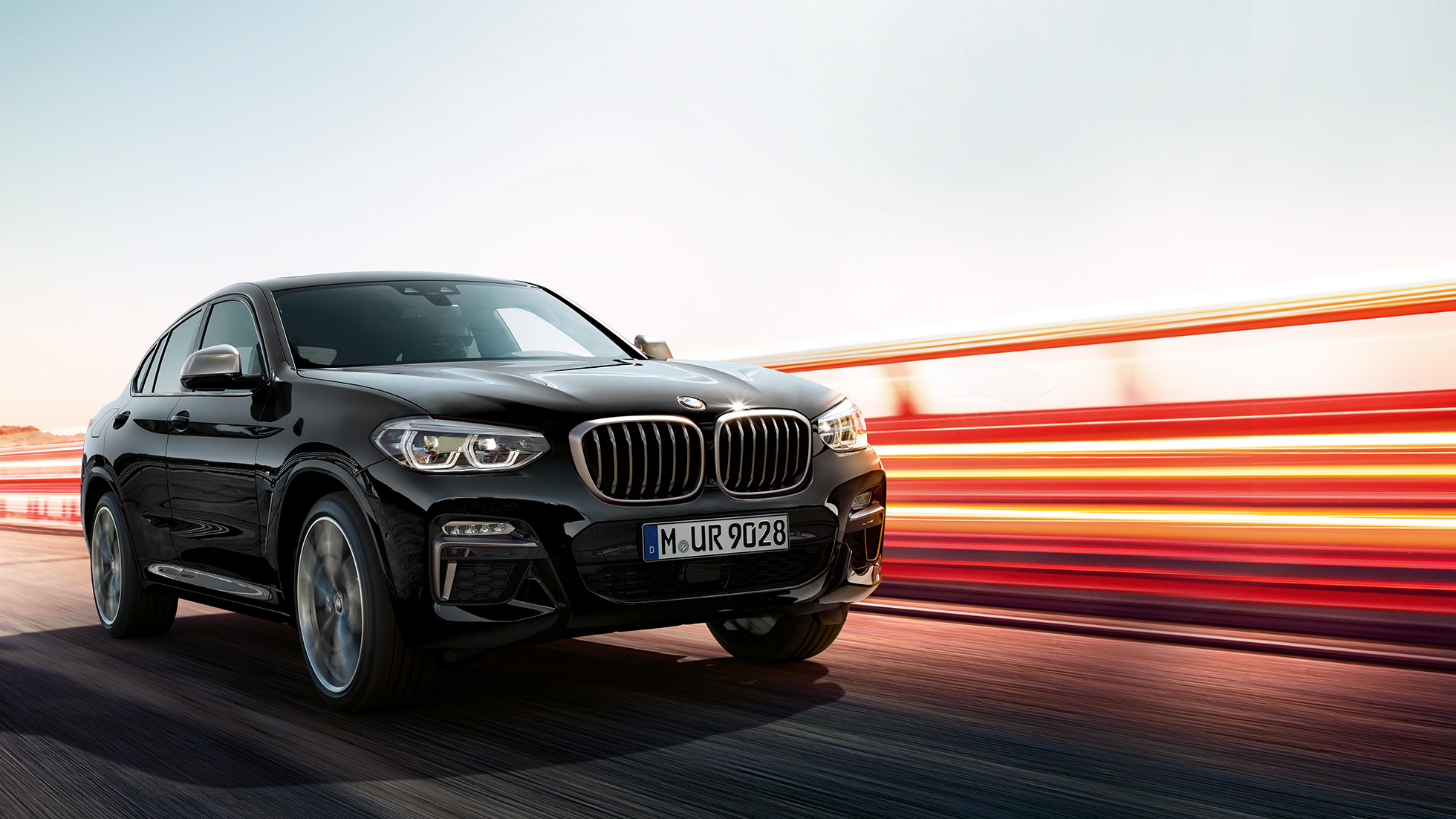 BMW X4 M40i, Dreiviertel-Heckansicht. BMW X4 M40i in Saphierschwarz metallic, fahrend, Exterieur, Dreiviertel-Heckansicht mit Lichtstreifen.