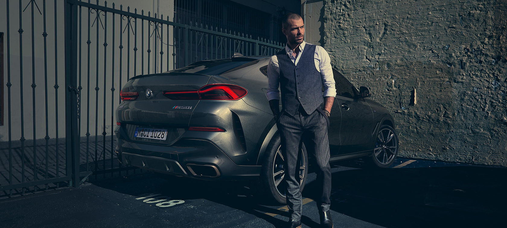 BMW X6 M50i in Dreiviertelheck-Ansicht. Mann steht neben BMW X6 M50i in Dreiviertel-Heckansicht.
