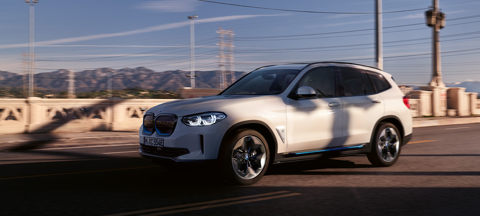 BMW iX3 G08 Dreiviertel-Frontansicht fahrend auf der Straße BMW iX3 G08 2020 Mineralweiß metallic Dreiviertel-Frontansicht fahrend auf der Straße