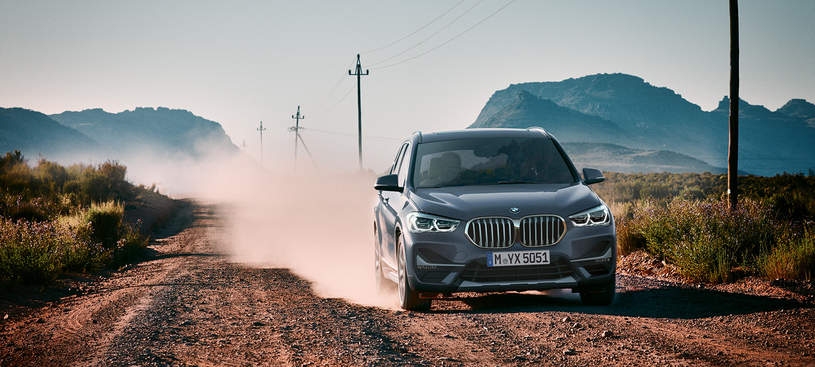 BMW X1, Dreiviertel-Heckansicht. BMW X1, Dreiviertel-Heckansicht fahrend vor Gebirgskulisse.