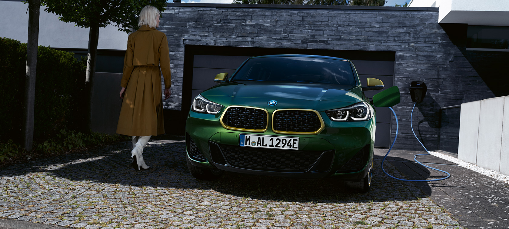 Frontansicht in Ladesituation mit Model links BMW X2 F39 Sanremo Green metallic