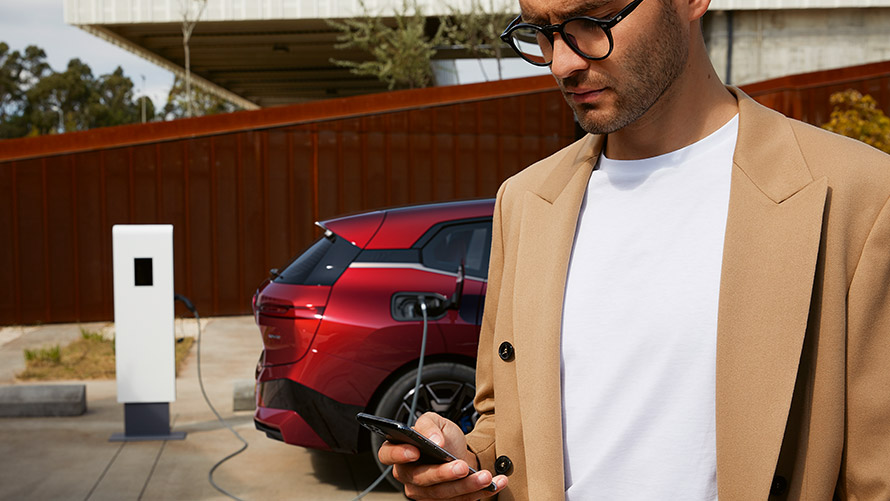 Mann mit Smartphone vor BMW iX an Ladestation Mann mit Smartphone vor BMW iX an Ladestation