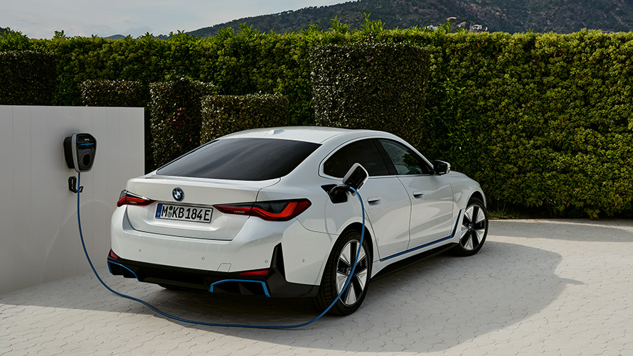 Laden an der BMW Wallbox Gen 3 BMW i4 G26 BEV Dreiviertel-Heckansicht BMW i4 G26 BEV Dreiviertel-Heckansicht ladend an der BMW Wallbox Gen 3 vor Hecke