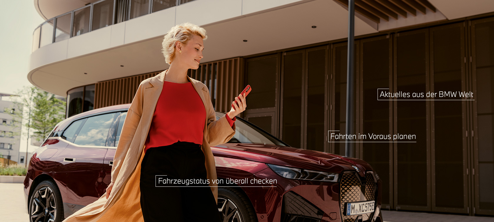 Frau steht vor weißem BMW X5 und benutzt My BMW App auf Smartphone Frau steht vor weißem BMW X5 und benutzt My BMW App auf Smartphone
