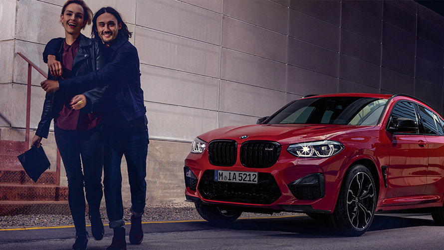Eine Frau und ein Mann gehen lachend vor einem BMW. Eine Frau und ein Mann gehen lachend vor einem BMW.