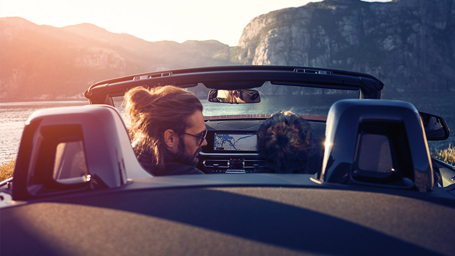 Ein Mann und eine Frau sitzen in einem BMW-Cabrio vor einer Berg- und Seenlandschaft. Ein Mann und eine Frau sitzen in einem BMW-Cabrio vor einer Berg- und Seenlandschaft.