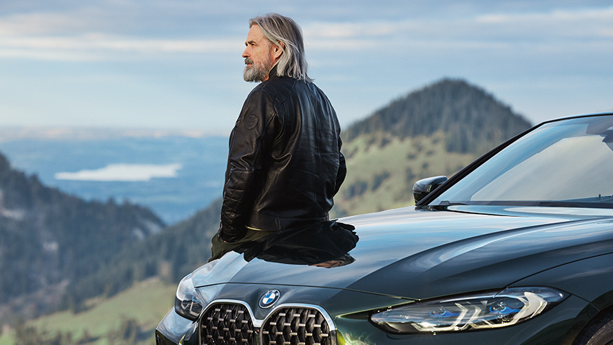 Mann lehnt an einem BMW vor Berglandschaft BMW Frühlings- und Sommerzubehör Mann lehnt an einem BMW vor Berglandschaft