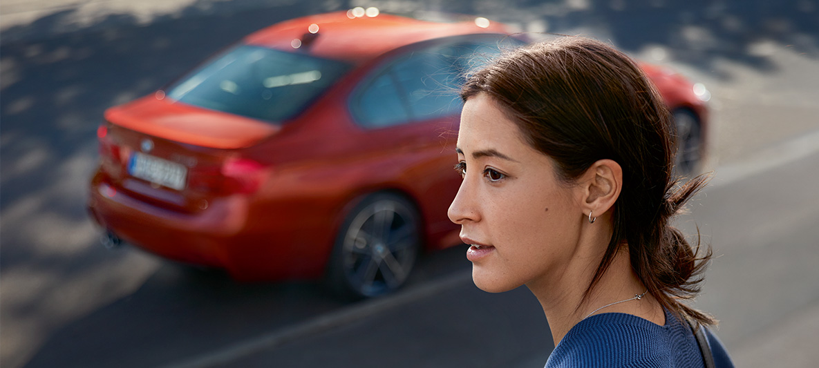 Eine Frau sieht in die Ferne. Hinter ihr fährt ein BMW entlang. Eine Frau sieht in die Ferne. Hinter ihr fährt ein BMW entlang.