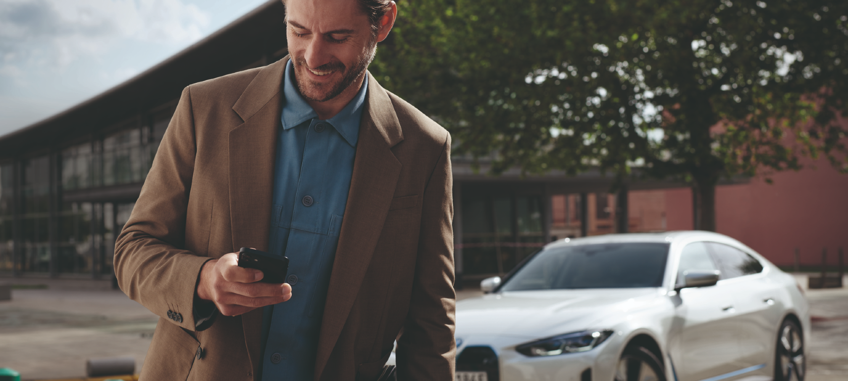 Ein eleganter Mann blickt vor einem BMW auf sein Handy. Ein eleganter Mann blickt vor einem BMW auf sein Handy.