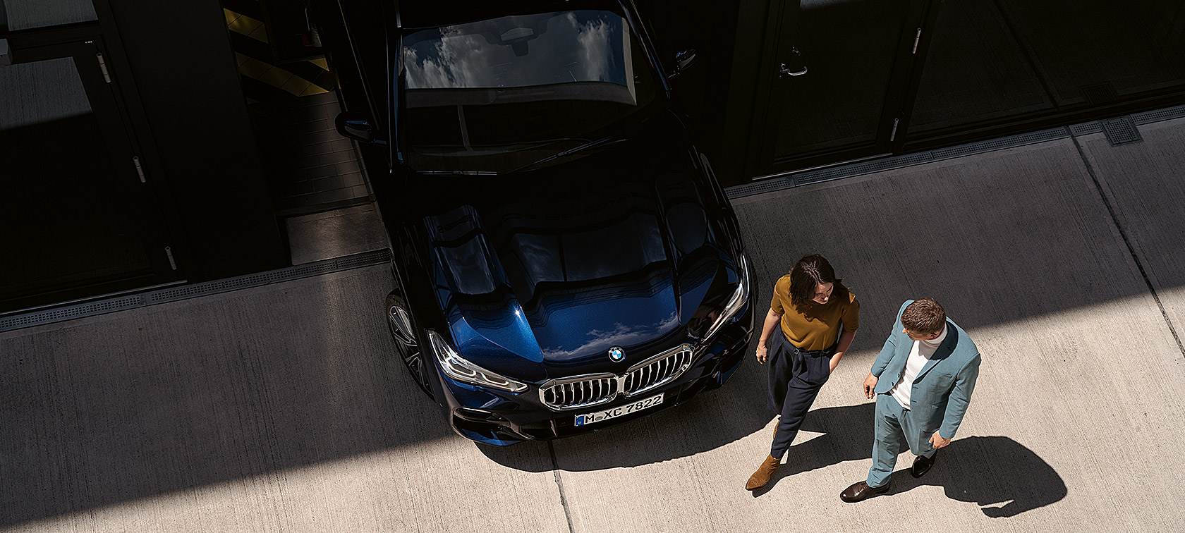 Eine Frau und ein Mann spazieren an der Front eines BMW vorbei. Eine Frau und ein Mann spazieren an der Front eines BMW vorbei.