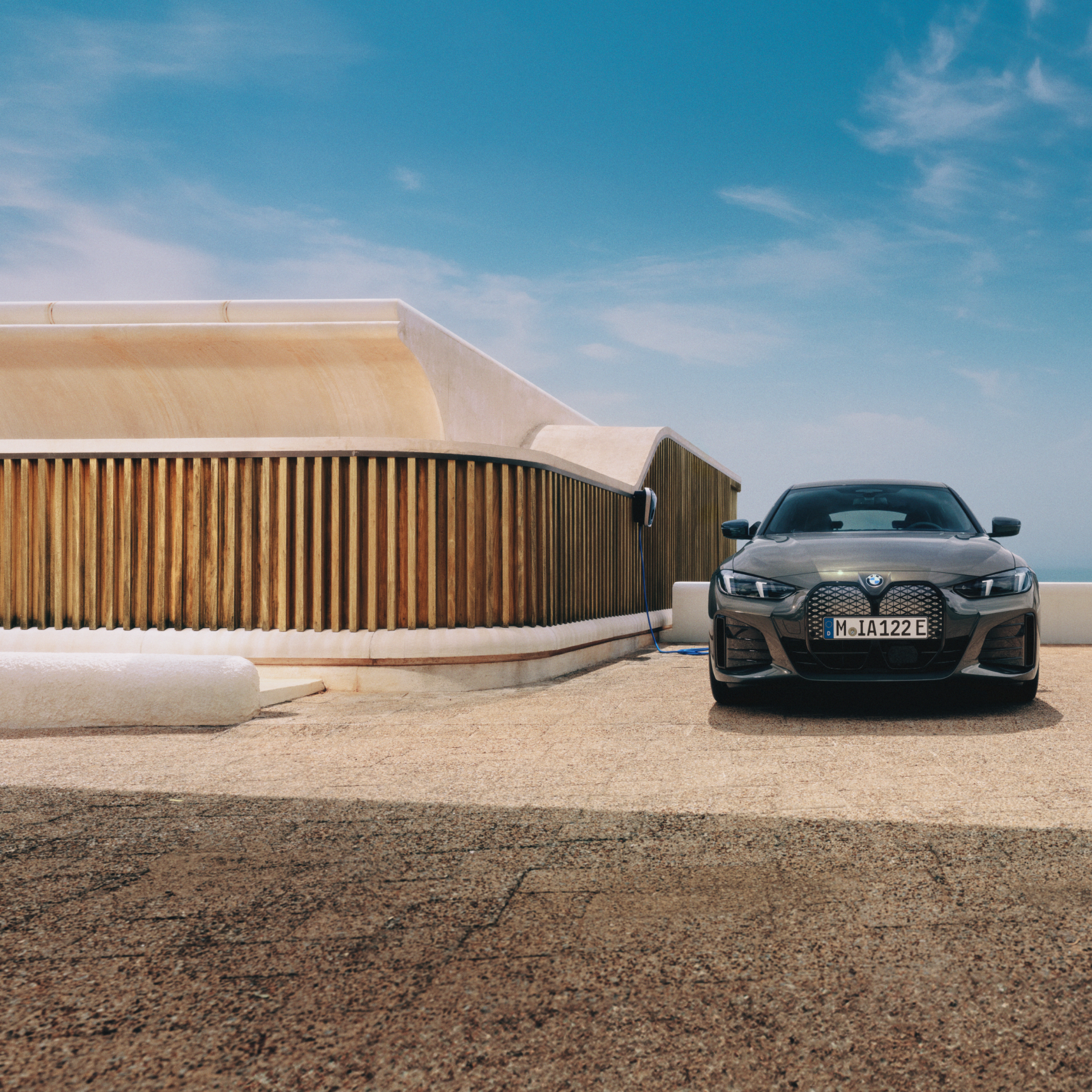 Ein Mann mit einem Smartphone steht neben einem BMW i4, der an einer Wallbox angeschlossen ist