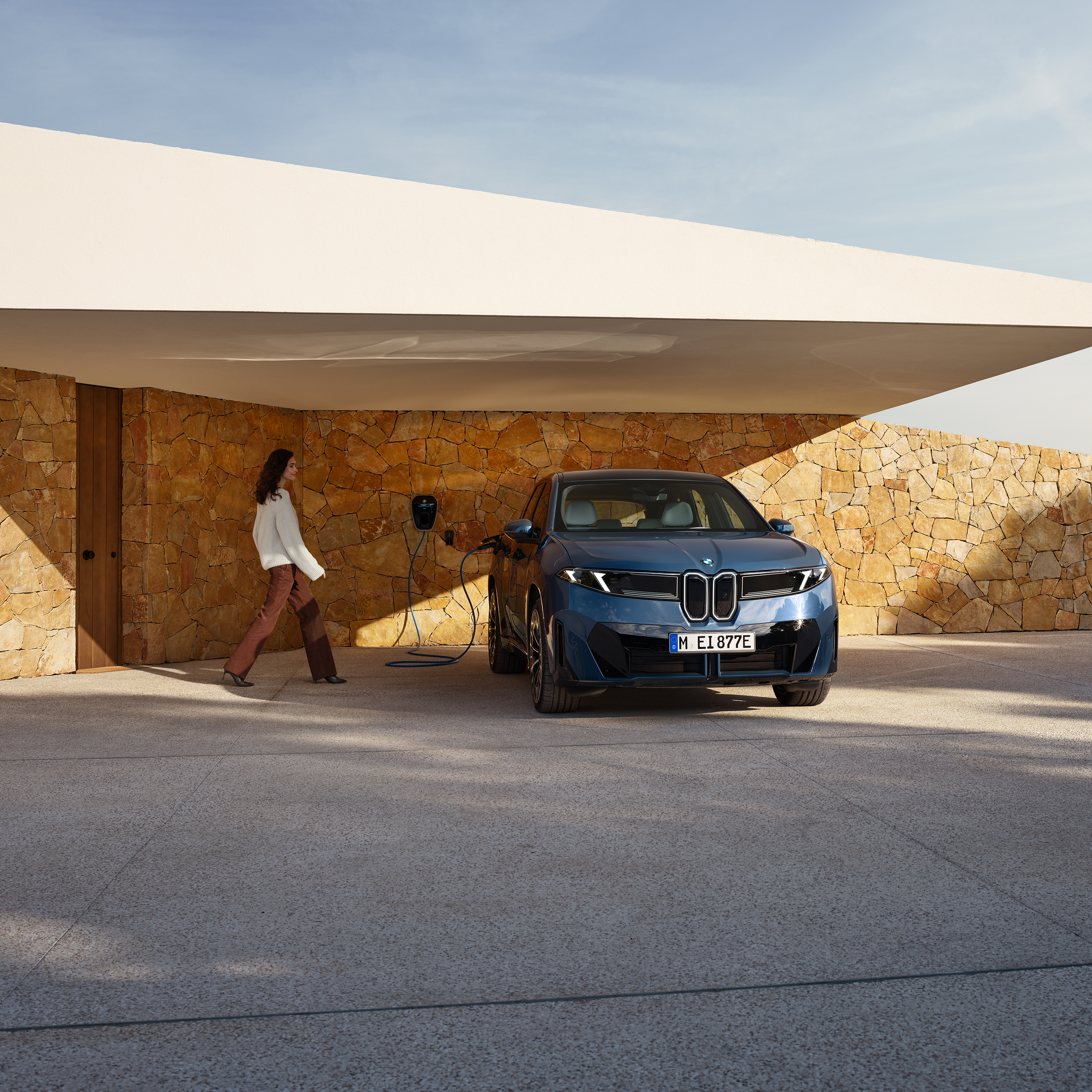 Eine Frau geht auf einen BMW iX3 zu, der an einer Wallbox angeschlossen ist