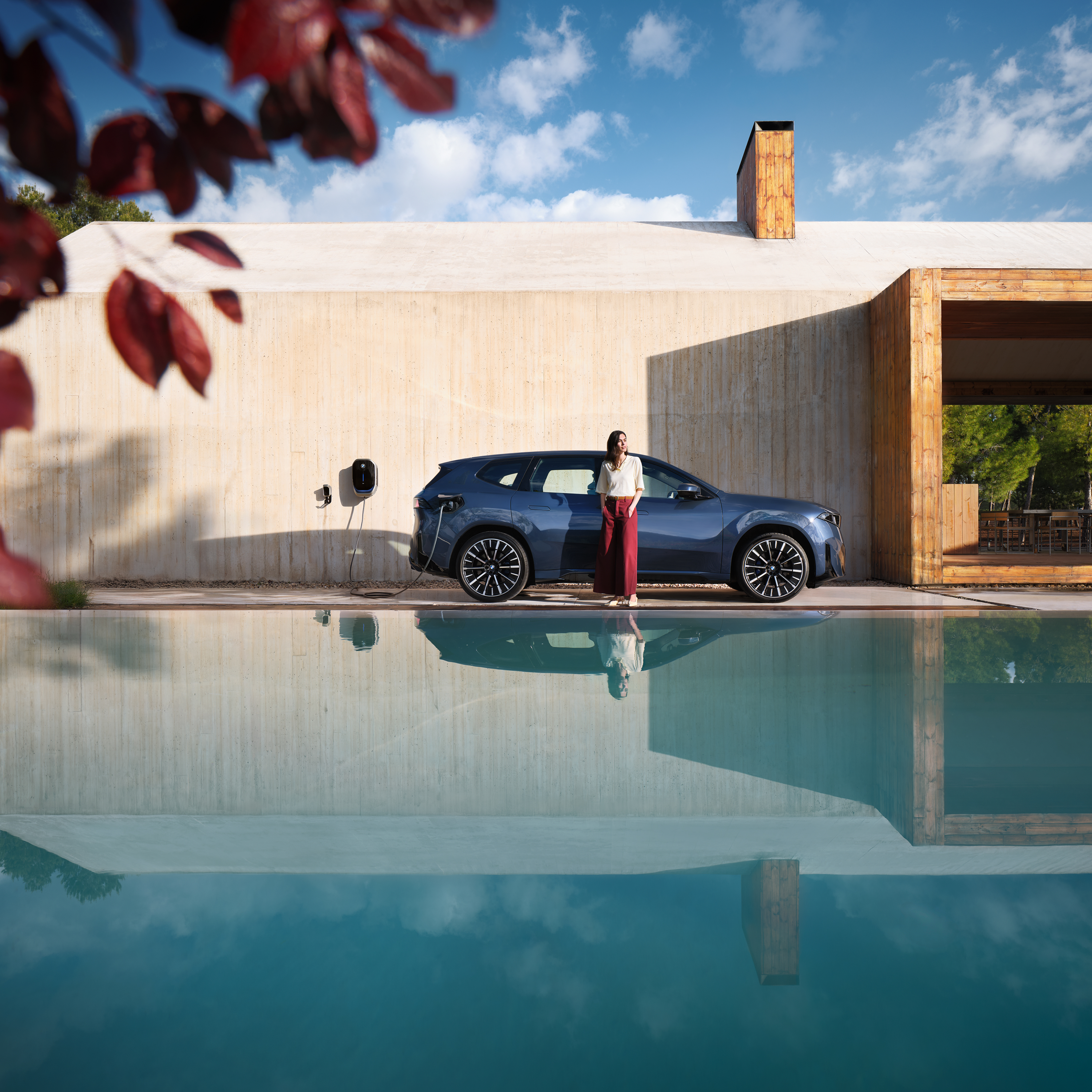 Eine Frau steht vor einem BMW iX3 der an einer Wallbox angeschlossen ist