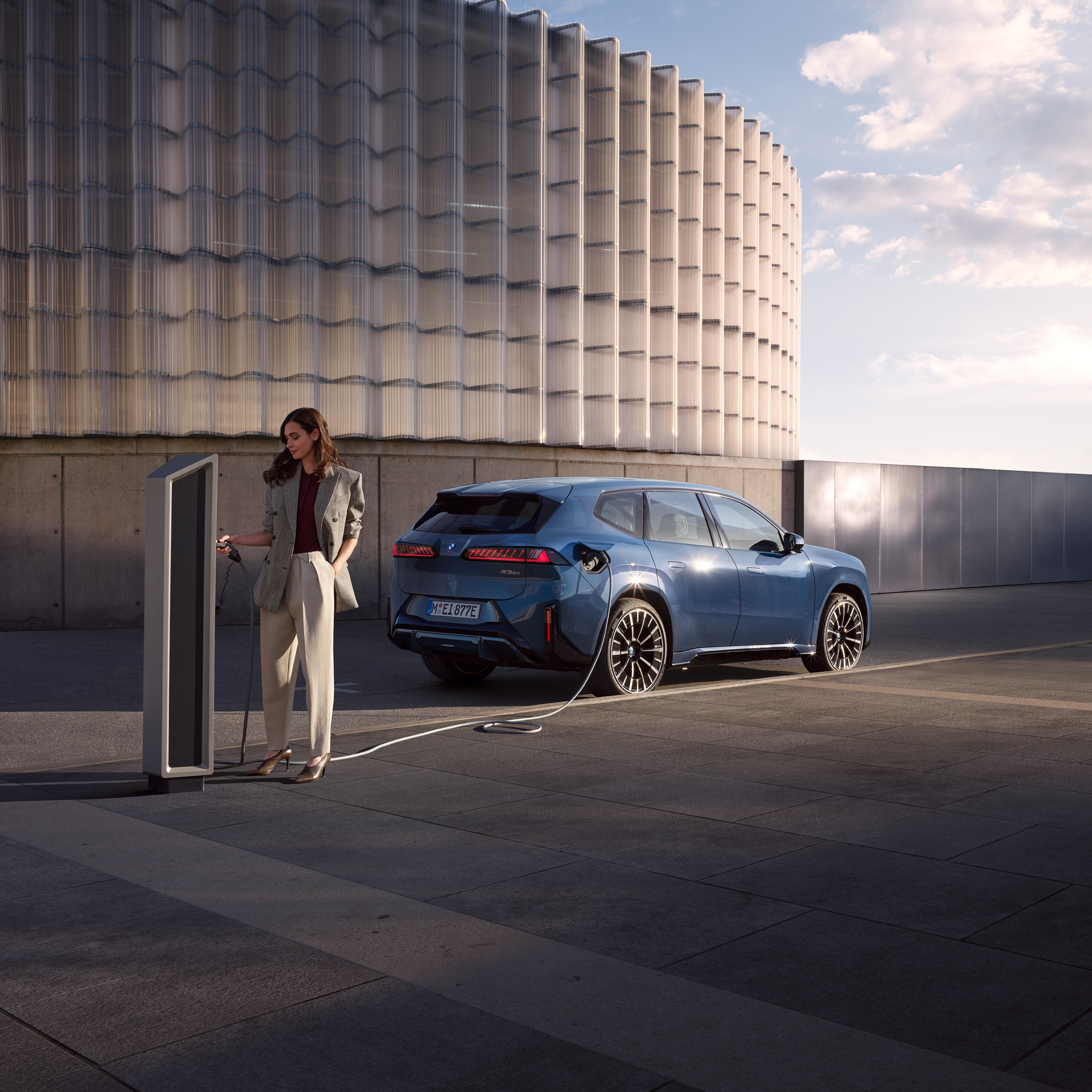 Eine Frau steht neben einem BMW iX3, der an einer öffentlichen Ladesäule angeschlossen ist