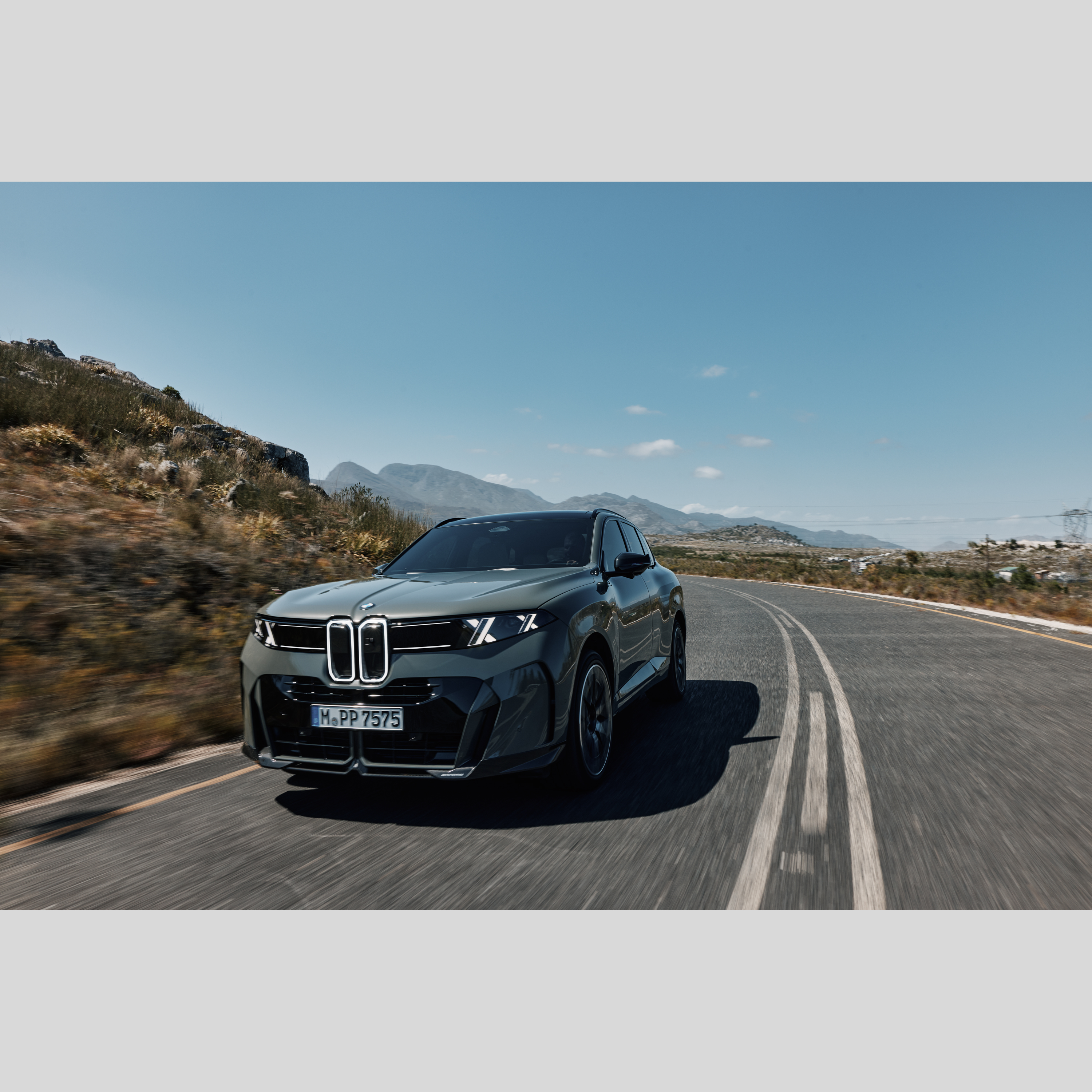 BMW iX5 in Fahrt auf kurviger Bergstraße bei Sonnenuntergang