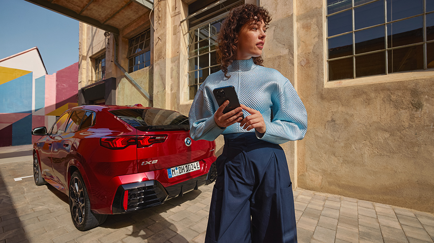 Eine Frau blickt vor einem BMW auf ihr Handy.