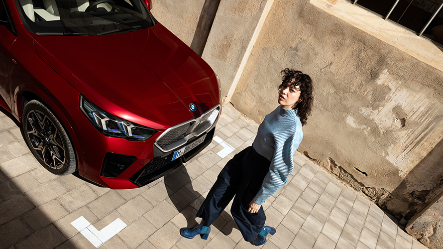 Eine Frau geht um einen roten, elektrischen BMW. Eine Frau geht um einen roten, elektrischen BMW.