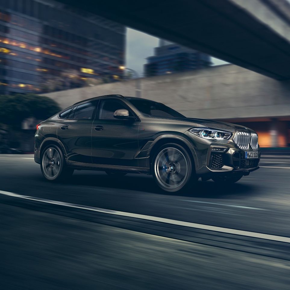 BMW X6 driving. BMW X6 in Dreiviertel-Front-Perspektive fahrend vor urbaner Kulisse.